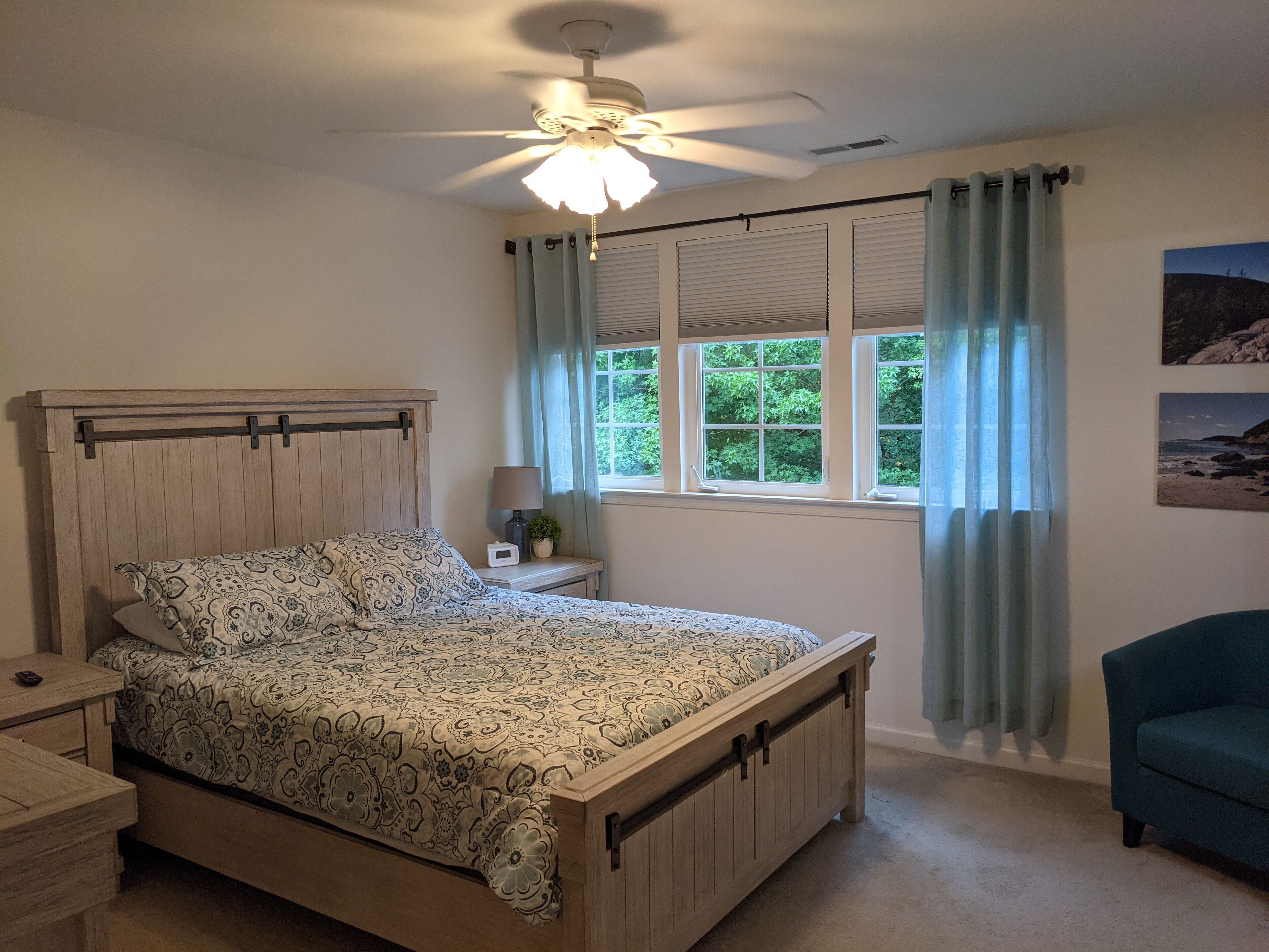 A bedroom with a wooden bed, a nightstand, a lamp, a ceiling fan, and a window with curtains.