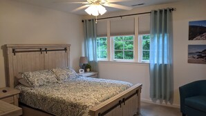 Quarto com cama de madeira, mesa de cabeceira, luminária, ventilador de teto e janela com cortinas.