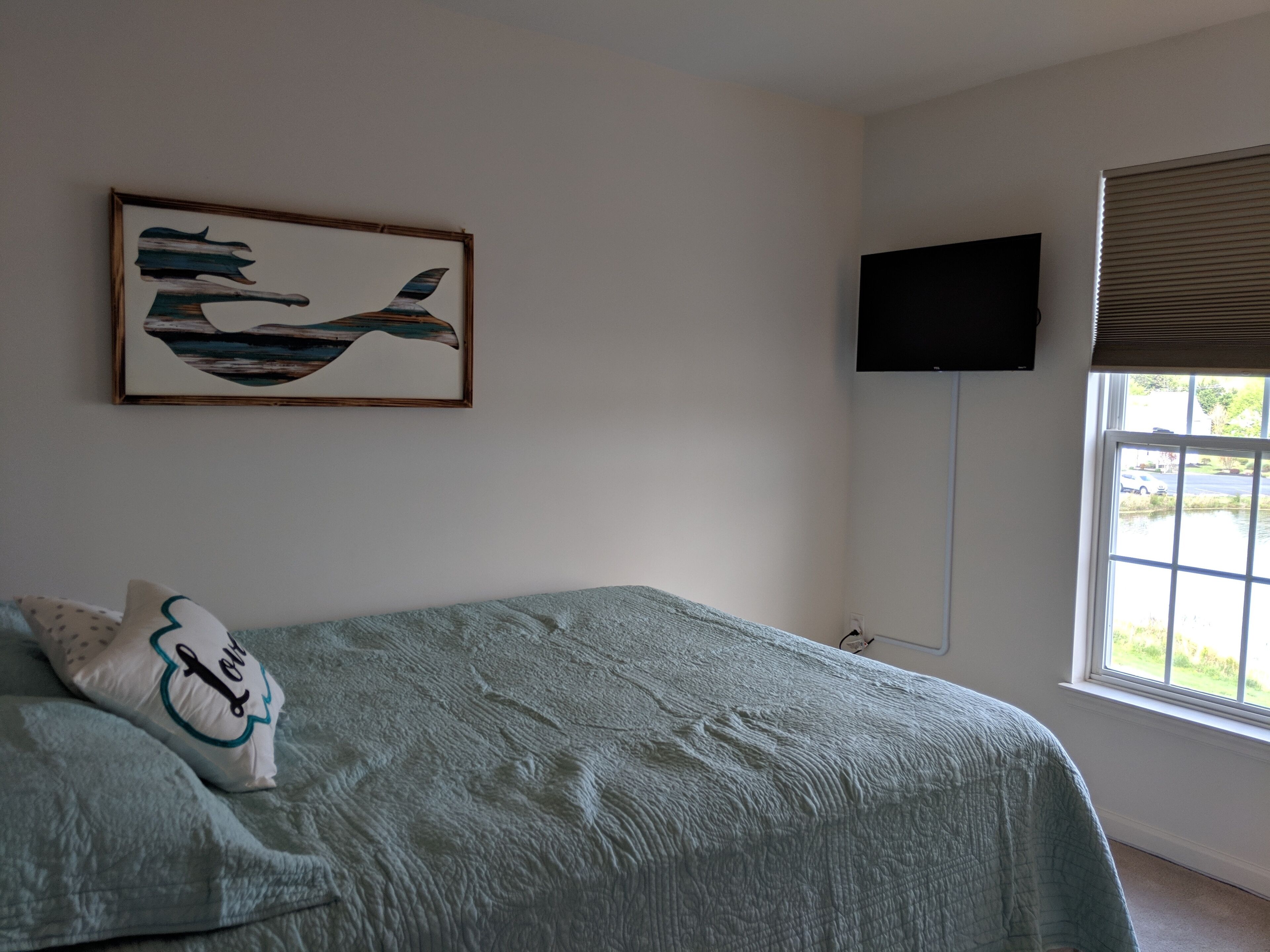 Un dormitorio con cama, un cuadro, un televisor y una ventana.