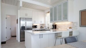 Cozinha moderna com armários brancos, eletrodomésticos de aço inoxidável e uma ilha central com banquetas.