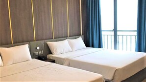 Et hotelværelse med to senge, et natbord med telefon og et vindue med gardiner.