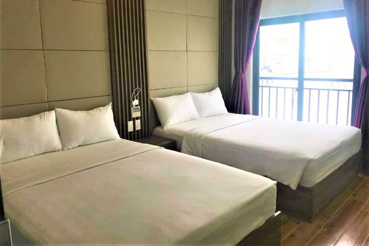 A hotel room with two single beds, a nightstand with a lamp, and a window with curtains.