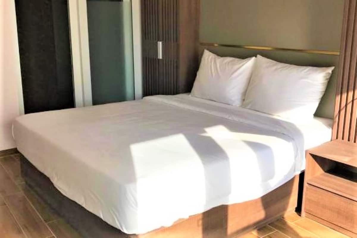 A neatly made bed with white linens in a room with a wooden headboard and a small wooden nightstand beside it.