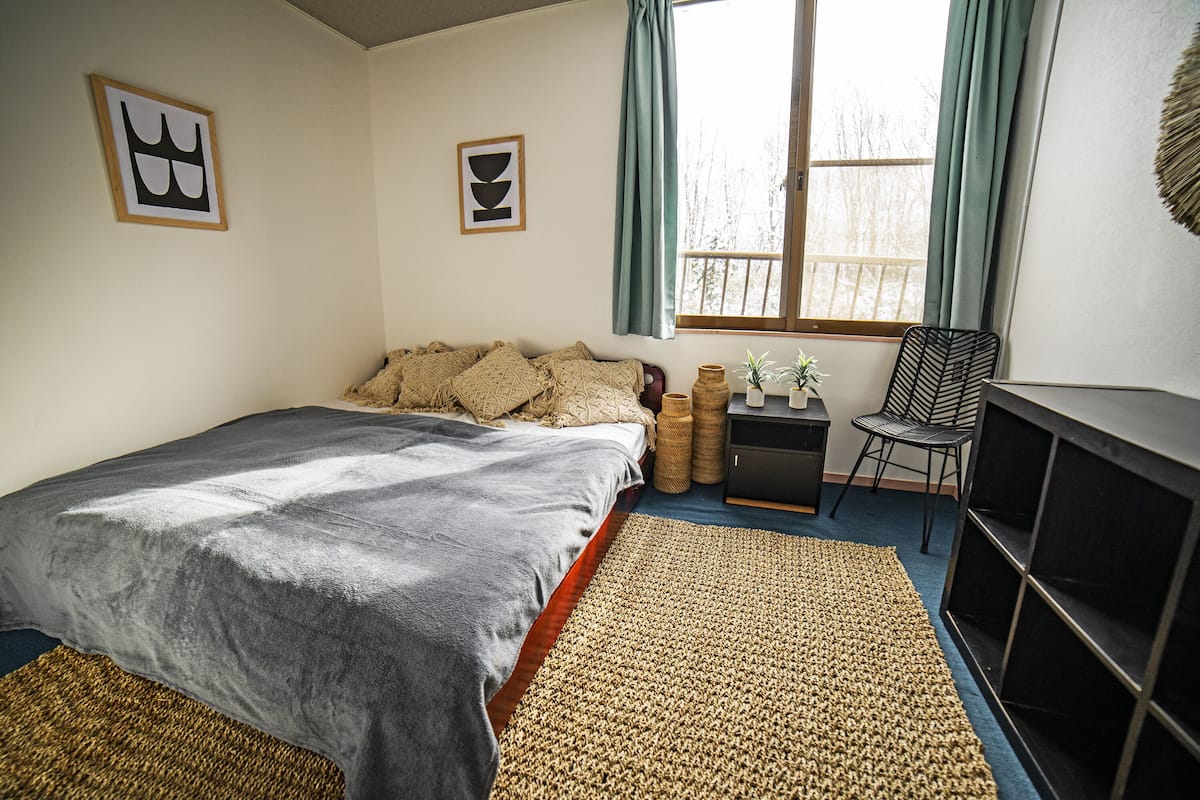 A bedroom with a bed, a desk, a chair, and a window with curtains.