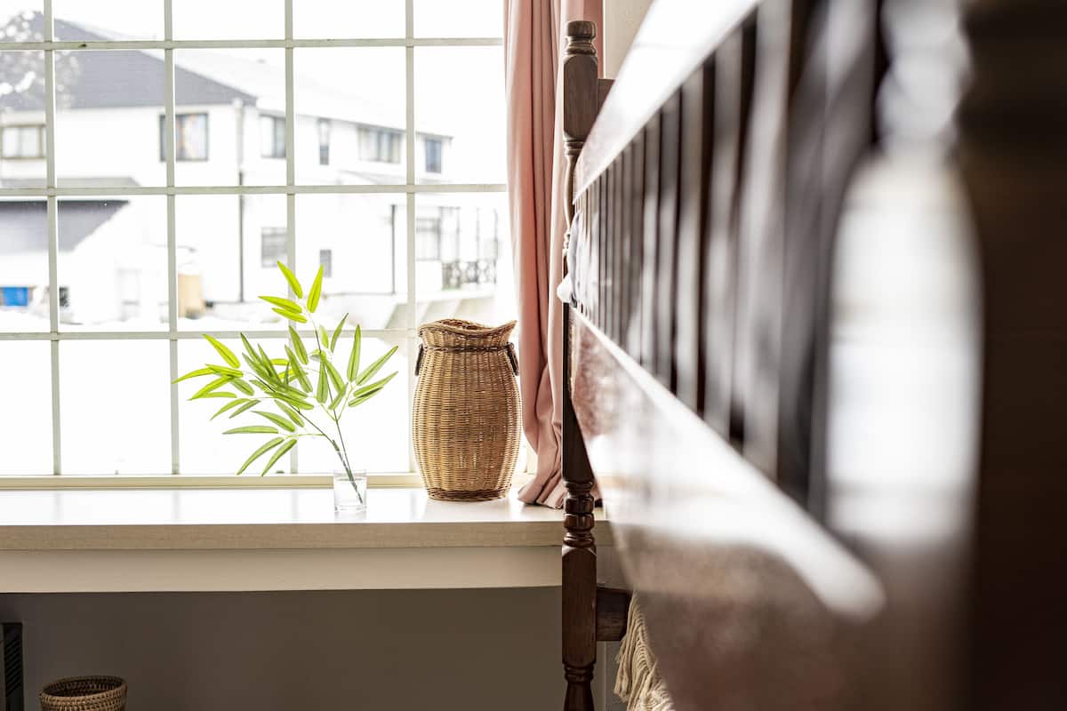 A window with a view of buildings outside, a wicker basket, and a potted plant on the windowsill.