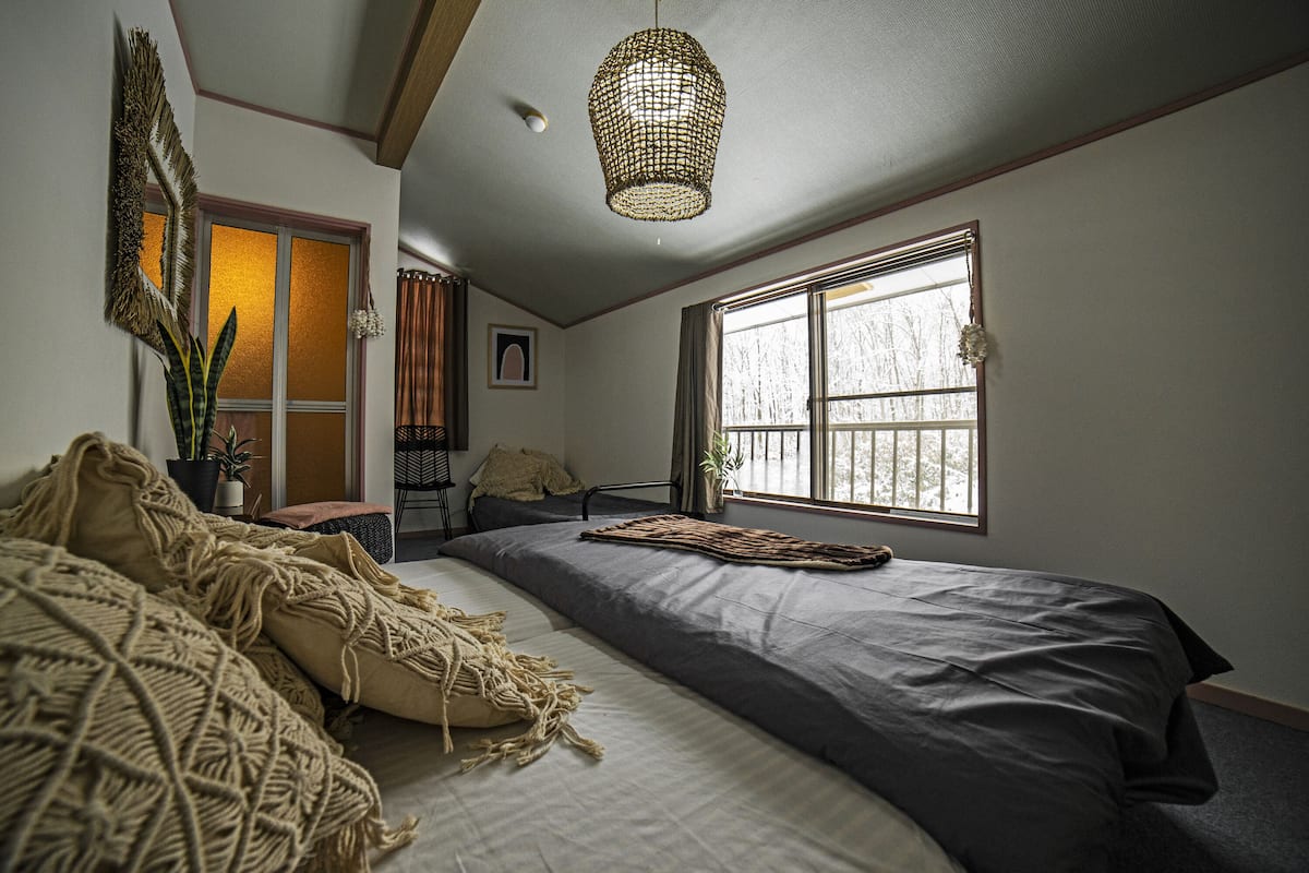 A bedroom with a large bed, a window with a view, a hanging light fixture, and a plant.