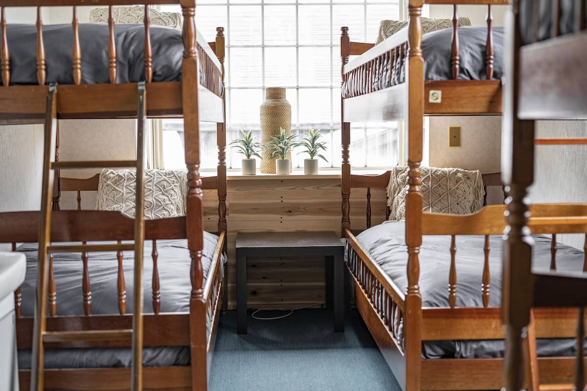 A bunk bed room with wooden frames, a small table, and potted plants.