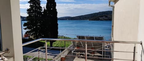 A balcony with a metal railing overlooking a body of water, a tree, and a distant hill.