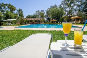 A pool area with lounge chairs, a covered seating area, and a glass of orange juice.