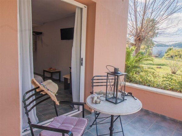 A balcony with a table and chairs, a view of greenery, and a door leading to an interior room.