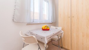 Ein kleiner Essbereich mit Tisch und Stühlen, ein Fenster mit durchscheinenden Vorhängen und ein Holzschrank.