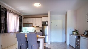 Una cocina moderna con armarios blancos, microondas y refrigerador. Hay un comedor con una mesa y sillas.