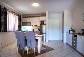 A modern kitchen with white cabinets, a microwave, and a refrigerator. There is a dining area with a table and chairs.