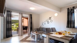 Una sala de estar moderna con sofá, mesa de centro y comedor. Tiene un balcón con cortinas, una pared con adornos circulares y una mesa de comedor preparada con platos, tazas y un croissant.