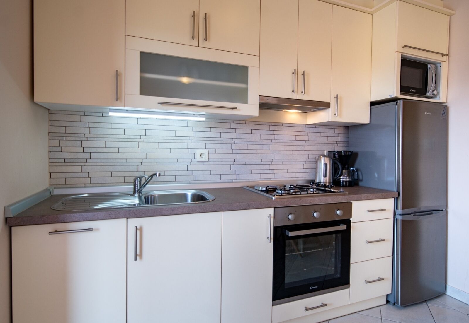 Eine moderne Küche mit weißen Schränken, einer Edelstahl-Spüle, einem Gasherd und einem eingebauten Backofen.