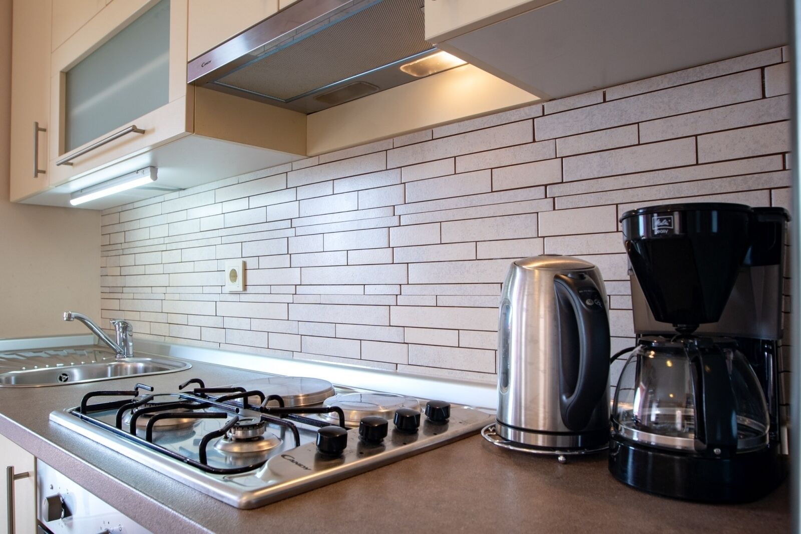 A kitchen with a gas stove, a kettle, and a coffee maker.