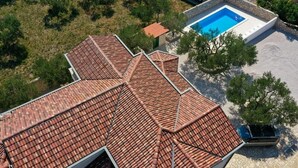 A rooftop with a terracotta tile roof, a swimming pool, and surrounding greenery.