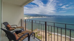 A balcony with wicker furniture overlooking a beach and ocean. - Grand Venetian Puerto Vallarta Beachfront Condo  (Puerto Vallarta)