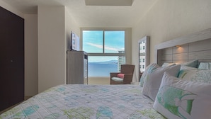 A bedroom with a large bed, a chair, and a view of the sea through a window. - Grand Venetian Puerto Vallarta Beachfront Condo  (Puerto Vallarta)