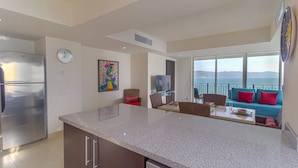 A modern kitchen with a stainless steel refrigerator, a dining area with a glass table, and a living room with a blue sofa and red pillows. - Grand Venetian Puerto Vallarta Beachfront Condo  (Puerto Vallarta)