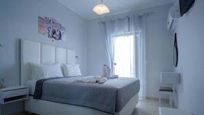 Un dormitorio con una cama, una mesita de noche, una silla, un televisor montado en la pared y un ventanal con cortinas.