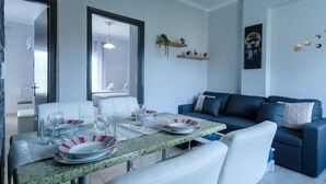 Una sala moderna con una mesa de comedor preparada para cuatro, sofás blancos y un sofá azul.