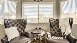 A room with two leather armchairs, a round table with two wine glasses, and a window with blinds.
