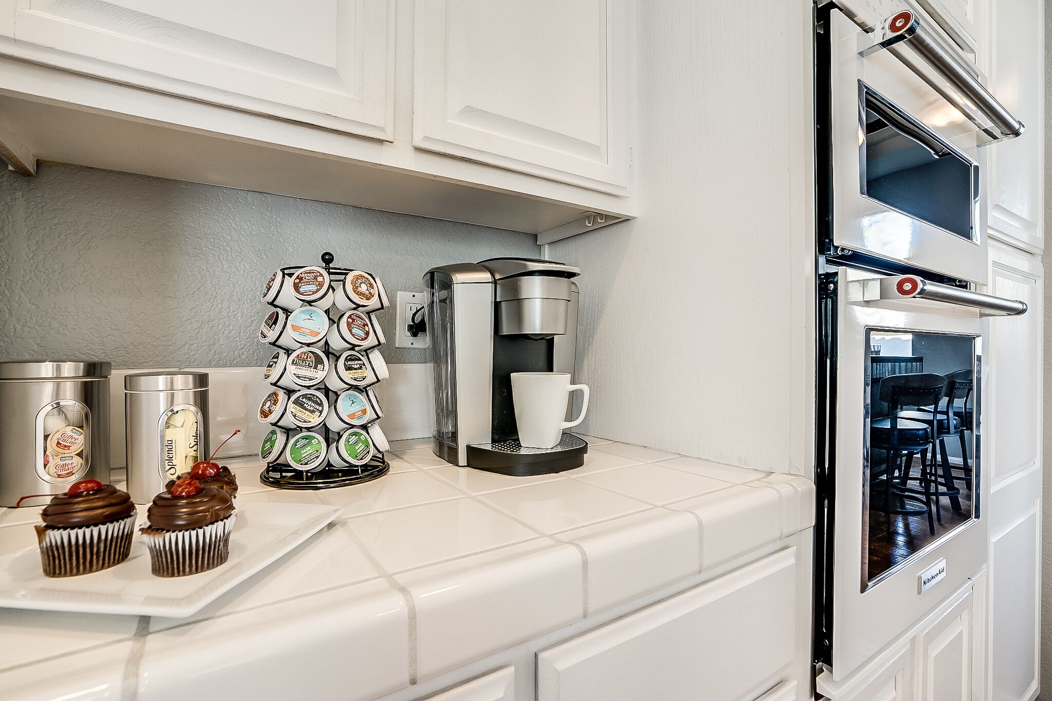 A kitchen with a coffee machine, a coffee cup, and a tray with cupcakes.