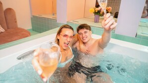 Un couple dans un jacuzzi, un verre de champagne à la main, entouré d’un intérieur moderne agrémenté d’un éclairage en arc de cercle.