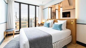 Une chambre d’hôtel avec un grand lit, un bureau, une chaise et une vue sur la Tour Eiffel.