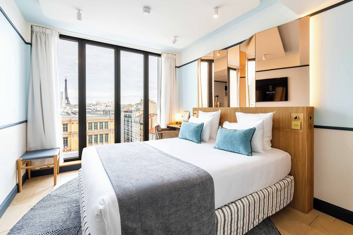 A hotel room with a large bed, a desk, a chair, and a view of the Eiffel Tower.
