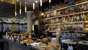 Un espace bar avec des étagères remplies de bouteilles d’alcool, une machine à café et un assortiment de viennoiseries et de pains.