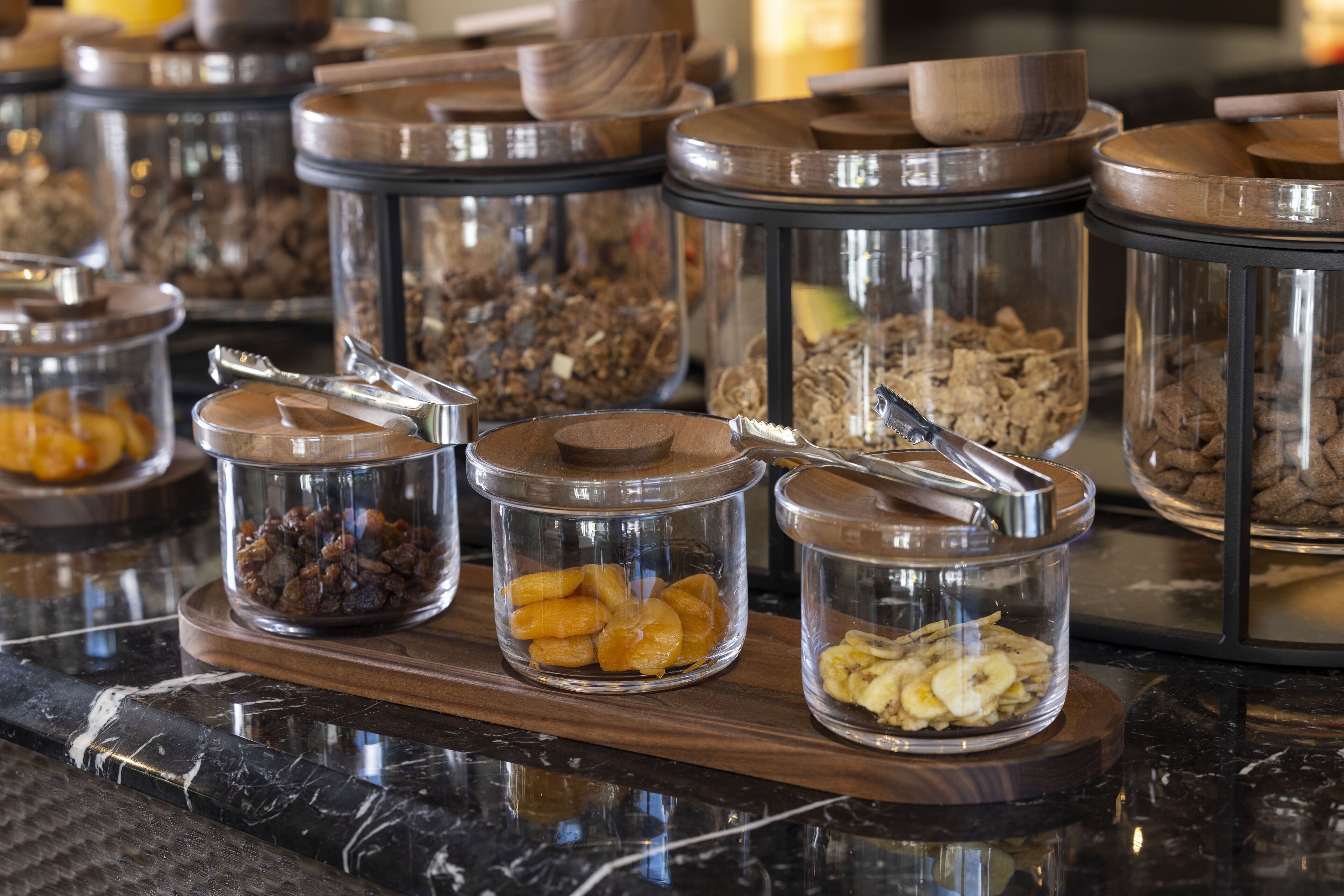 A buffet with various food items in glass containers with lids, arranged on a wooden board.