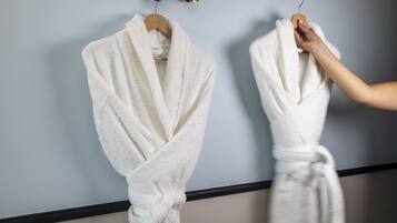 Two white bathrobes hanging on a wall, one on a wooden hanger and the other on a metal hook.