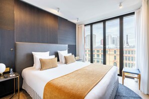A modern hotel room with a large bed, a nightstand, a chair, and a view of the Eiffel Tower. - Quinzerie Hotel (Paris)