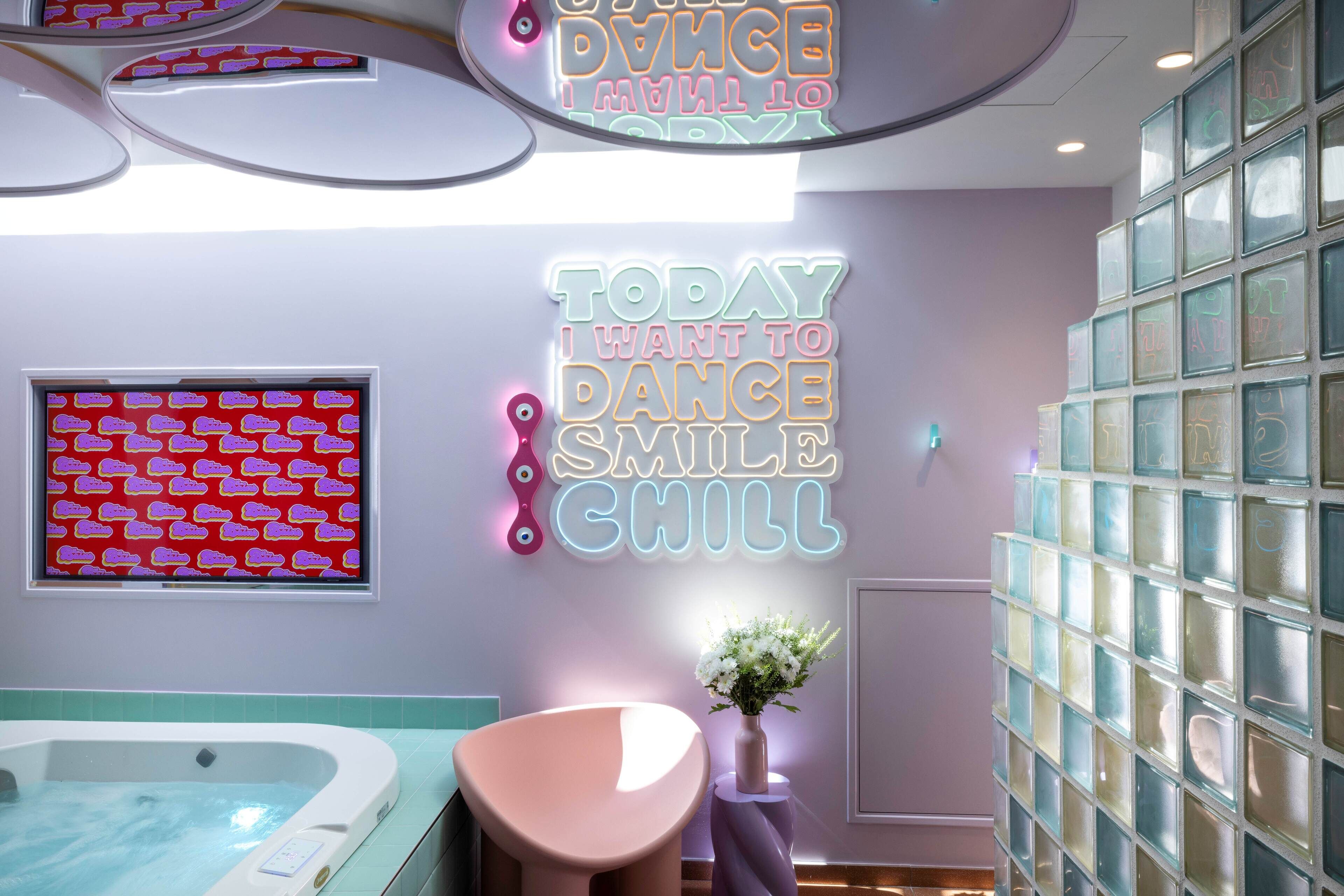 Ein Wellnessraum mit Whirlpool, einem rosafarbenen Sessel und einer Wand mit Neonreklamen.