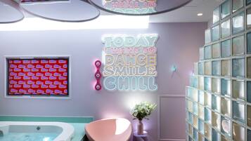 Ein Wellnessraum mit Whirlpool, einem rosafarbenen Sessel und einer Wand mit Neonreklamen.