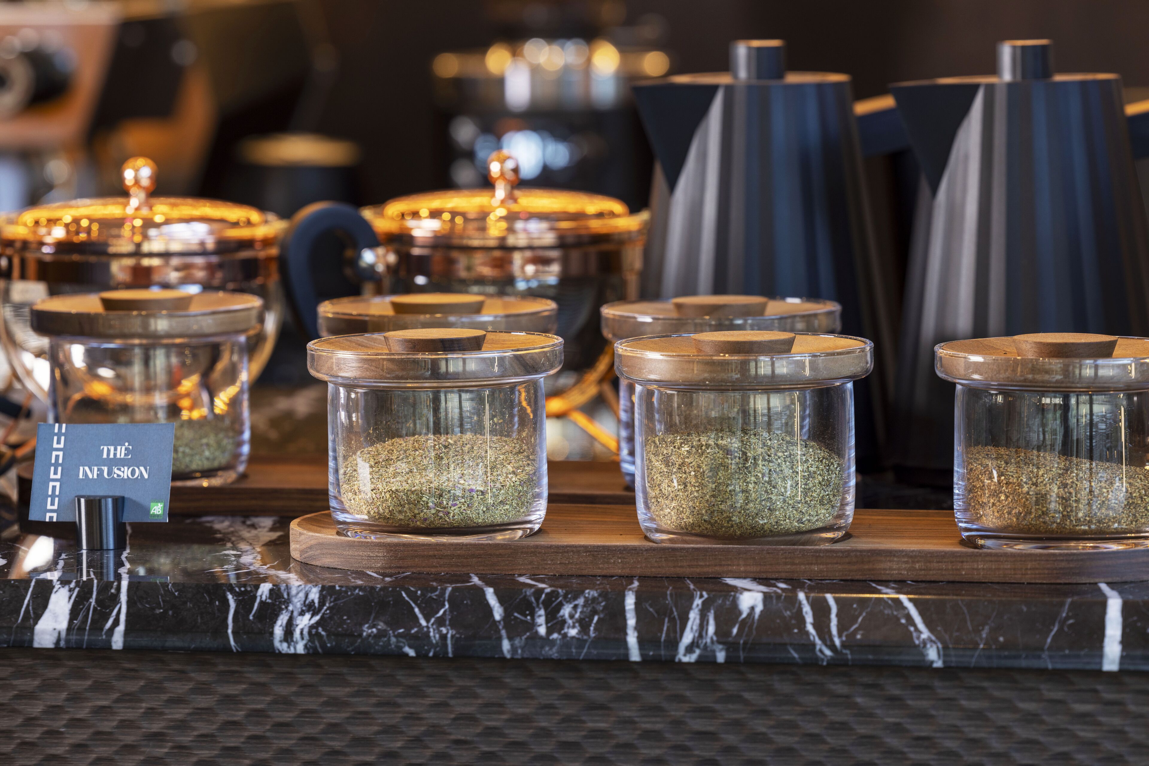 A display of glass containers with lids, each containing a different type of seasoning, arranged on a wooden board.