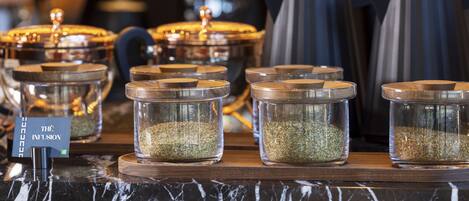A display of glass containers with lids, each containing a different type of seasoning, arranged on a wooden board.