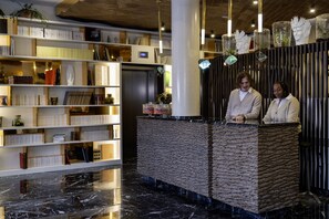 A reception area with a marble floor, a reception desk, and a bookshelf filled with books and decorative items. - Quinzerie Hotel (Paris)
