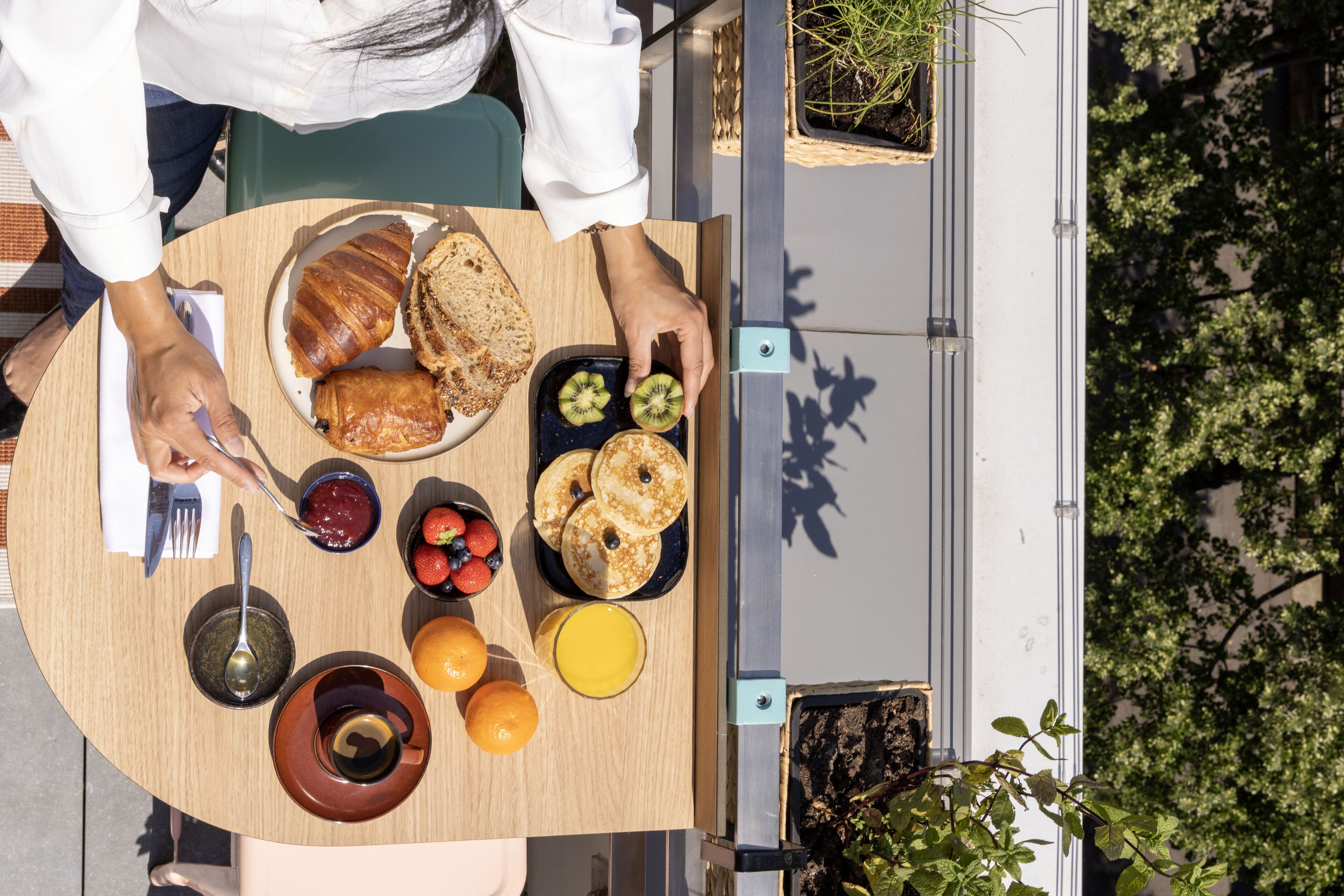 A breakfast table with croissants, kiwi slices, strawberries, and orange juice.