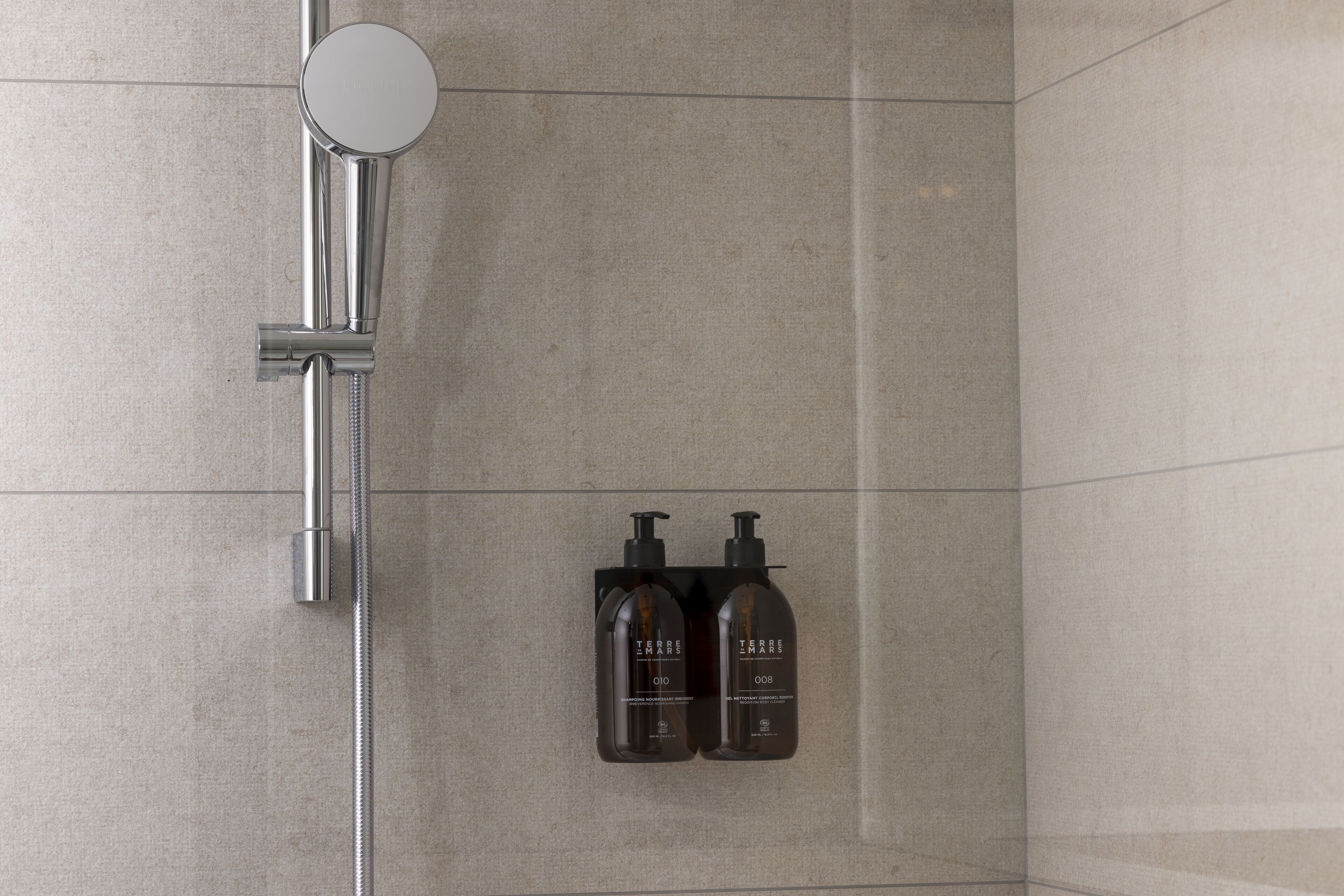 Zona de ducha con cabezal de ducha manual y dos botellas de gel de baño Terre de Mars.