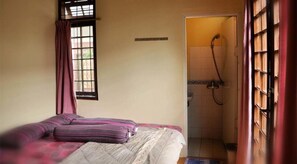 Una habitación pequeña con cama individual, ventana, zona de ducha y cortina.