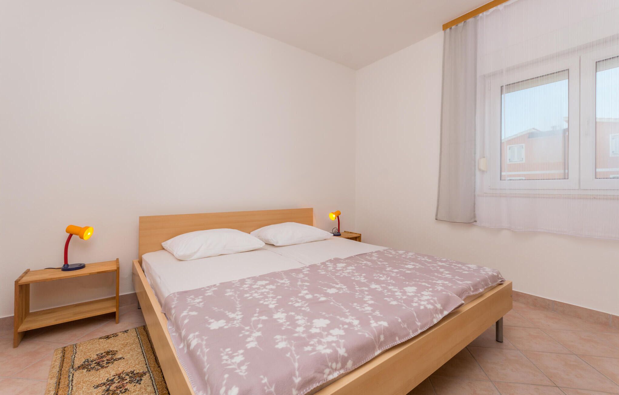 A bedroom with a wooden bed, two bedside tables, a night lamp, and a window with curtains.