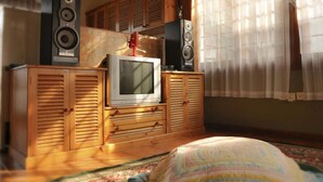 Ein Zimmer mit einem Fernseher auf einer Holzkommode, Lautsprechern an beiden Seiten und einem gemusterten Teppich auf dem Boden.