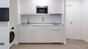 A compact kitchen with white cabinetry, a built-in oven, and a washing machine.