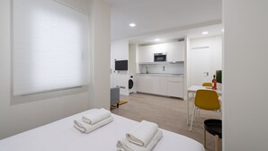 A modern hotel room with a bed, a small kitchenette, a dining area, and a bathroom.