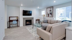 A modern living room with a fireplace, a flat-screen TV, a sofa, and a glass coffee table.