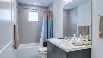 A modern bathroom with a bathtub, toilet, and vanity with a mirror.