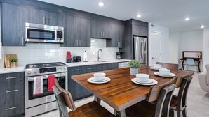 A modern kitchen with dark wood cabinets, stainless steel appliances, and a wooden dining table set for four.
